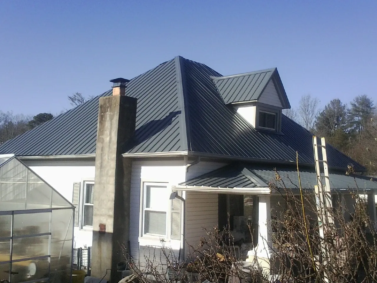 Dark blue standing seam metal roof on a white farmhouse with dormer — Slate & Tile Roof Repair by Roofing Brothers in Hamlin