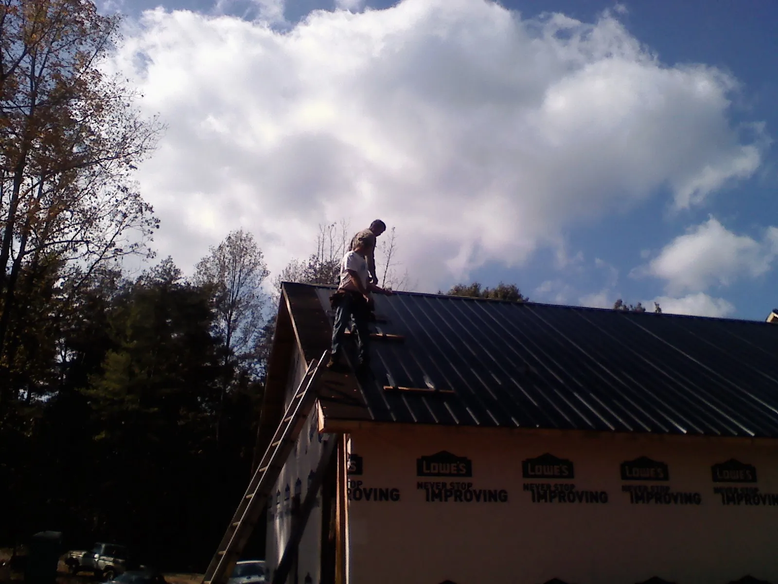 Roofer fastening dark metal panels high against a cloudy sky, from a Roof Inspection job in Hamlin