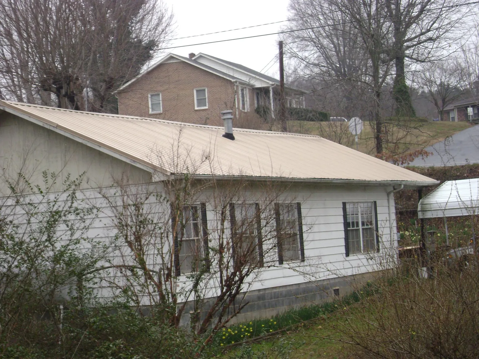 Tan metal roof on a white sided house set into a hillside — Commercial Roofing by Roofing Brothers in Hamlin